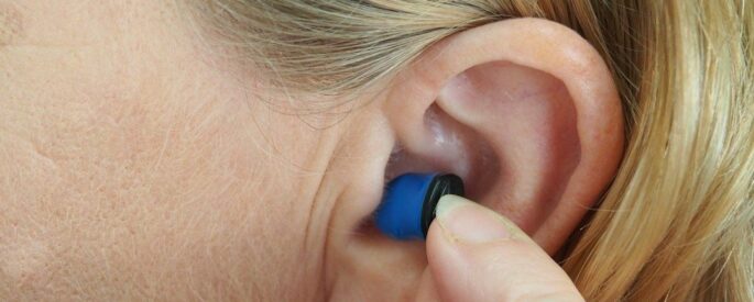 Nahaufnahme eines blauen Akustikfilters, der ins Ohr eingesetzt wird