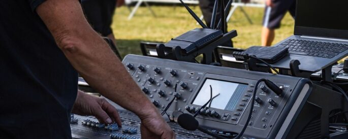 Tontechniker bedient Mischpult und Laptop bei einer Open-Air-Veranstaltung